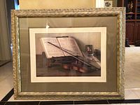 Photo of framed artwork showing violin, bow, sheet music, and a small framed photo of a man.