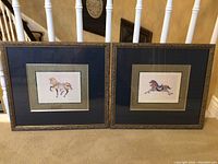 Front view of two framed decorative horse art prints together on carpeted floor, showing detailed frames and mats.