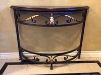Front view of demi-lune hall table showing wood top and ornamental wrought iron metal base with gold highlights.