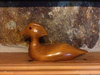 Side and front views of the handcarved wooden duck decoy showing the grain, shape, and features such as the red eyes and feather carvings.