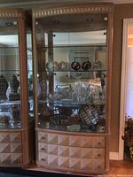 Front view of American Drew lighted display cabinet with glass shelving and wood drawer section below.