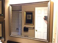 Front view of the rectangular wall mirror reflecting a bathroom and door, showing frame and glass condition clearly