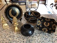 Front view of the black and gold decorative plates, bowls, small pot, and gold figurines on granite countertop