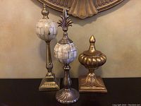 Set of three decorative finials showing variety of shapes and finishes including faux marble and gold-tone metal.