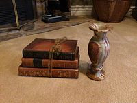 Three stacked vintage style books tied with brown measuring tape ribbon next to small stone/marble vase