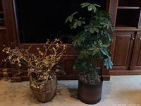 Two decorative plant items side by side; leafy green plant in black pot and yellow faux branches in basket-style pot.