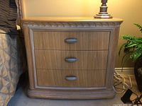 Front view of a wooden side table with three drawers, showing carved decorative border and dark handles.