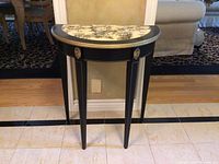 Front view of demi lune table showing black legs, gold accents and decorative medallions