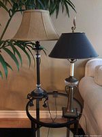 Pair of two table lamps on a round glass and metal side table near a beige sofa and plant, showcasing overall size and detailing.