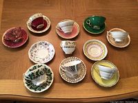Photo showing an overhead view of multiple assorted teacups paired with matching or mismatched saucers on a wooden surface, highlighting variety in shape, color, and pattern.