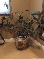 Full view photo of large vintage ceramic vase with artificial floral arrangement, showing intricate gold and beige design and branches with leaves and rosehip berries.