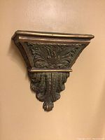 Close-up side view of decorative wall shelf with prominent leaf carvings and gold accents.