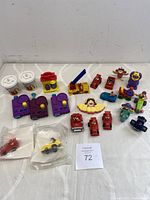 Full array of assorted McDonald's promotional figurines and toys showing small containers, figurines of Ronald McDonald, Hamburglar, Grimace, and various playset accessories, including purple lock boxes and miniature vehicles.