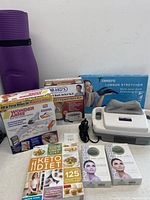 Photo displaying the fitness set including boxes of Dr. Ho's back relief belt, Wonder Arms workout system, Tobree lumbar stretcher, The Keto Diet book, two jade rollers, and a purple rolled yoga mat.