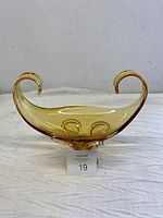 Front view of the gold amber colored art glass bowl showing the curled handles and elongated shape.