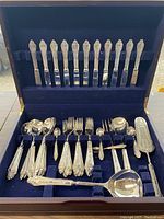Full open case showing top row of 12 dinner knives and bottom trays of forks, spoons and serving pieces on blue velvet lining.