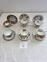 Lot overview showing all six bone china teacup sets with diverse floral and decorative patterns arranged on a white cloth