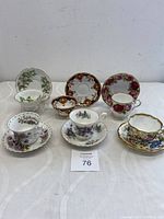 Photo of all six bone china teacup and saucer sets arranged on table showing varied floral patterns and gold trims.