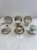 Overview photo showing six distinct matched bone china teacup and saucer sets arranged on a white surface, showcasing variety and condition of items.