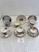 Six matched pairs of vintage bone china teacups with saucers showing floral and holiday-themed patterns, all placed on a white surface.