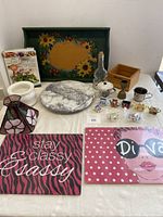 Table display with numerous kitchen items including hand painted tray, marble lazy Susan, stained glass lamp shade, decorative signs and small ceramics.