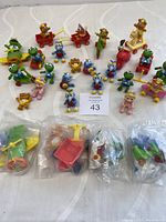 Photo showing a variety of Muppet Babies figurines on riding toys and scooters, plus some loose in plastic bags.