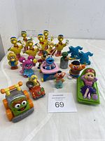 Lot of 19 Sesame Street character figurines including Big Bird, Miss Piggy, Oscar the Grouch, Cookie Monster, Ernie, and several blue Grover figures. They are arranged grouped, showing size scale and variety.