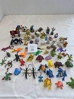 Wide view of assorted plastic animal figurines displayed on a white cloth including insects, frogs, dogs, horses and other animals.