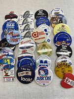 Lot of 32 advertising and collector's souvenir buttons arranged on flat surface.
