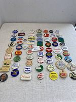 Overview of all 65 assorted souvenir pins arranged on a white surface showing variety in size, color, and design.
