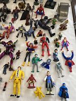 Overall view of the large mixed lot of superhero action figures showing a variety of figures including Spider-Man, Batman, and others on white surface.