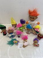 Front view of 14 troll dolls in various sizes with bright colored hair and some wearing clothes.