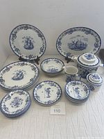 Complete lot of various blue and white stoneware items including plates, bowls, saucers, teapot, creamer, sugar and serving platter arranged on white cloth.