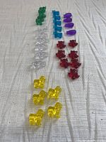 Multiple colorful translucent Crazy Bones game pieces arranged in rows on fabric. Colors include green, blue, purple, clear, red, yellow.