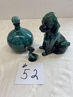 Three Blue Mountain Pottery pieces on white cloth: a round lidded vase, a sitting poodle figurine, and a small duck figurine.