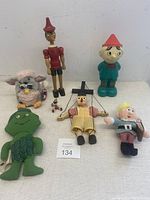 Lot including wooden Pinocchio marionette needing string repair, Furby toy, Green Giant plush, Island of Misfit Toys figures, and water bottle.