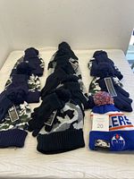 Photo of 10 matching sets of knit hats with camouflage pattern and navy blue gloves, plus one Edmonton Oilers branded toque with blue, orange, and white colors placed on a table.