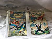Two comics side by side, Batman Family Giant on left and Superman Shazam on right, placed on fabric.