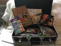 Wide view of the open black case showing multiple craft supplies, games, and coloring items with some packaging visible