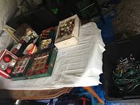 Overview of multiple boxes of glass Christmas ornaments and bins of lights on a table.
