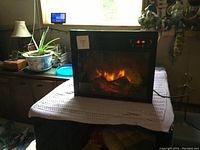 Electric fireplace heater unit on a covered table, showing flame simulation.