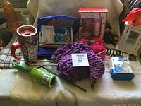 Various household items including a travel mug, yarn, fireplace bellows, gift sets, scarf, and wipes displayed on a couch.
