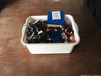 White tub filled with assorted Lego pieces on wooden floor