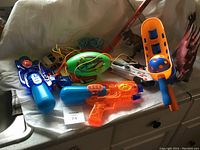 Photo of various outdoor toys including water guns, a ball launcher with a ball, a green foam football, and toy suction dart guns with wires.