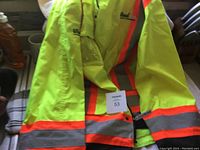 Bright yellow high-visibility safety coat with reflective orange and gray stripes, laid out on a surface. Snap buttons visible on sleeves.