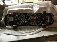 Side view of skateboard showing skeleton graphic on black deck and orange wheels placed on a kitchen counter.