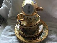 Photo showing stacked cups, saucers, and plates with a hand painted grapevine design in warm colors.