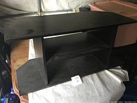 Front view of small black TV stand showing top surface and open middle shelf with dust accumulation.