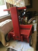 Small red wooden pull wagon from side angle showing handle, four white spoked wheels with black tires, and rectangular bed.