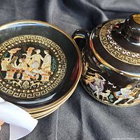 Close-up photo showing detailed depiction of classical Greek figures and decorative patterns on ceramic pieces